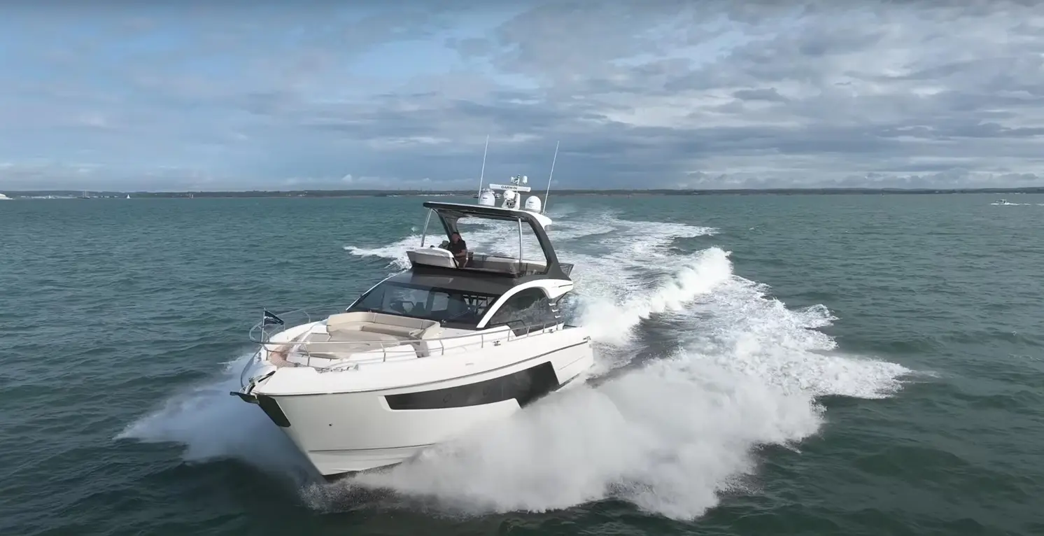 Luxury motorboat speeding through turquoise waters, leaving a wake and driven by a person on deck under a cloudy sky.